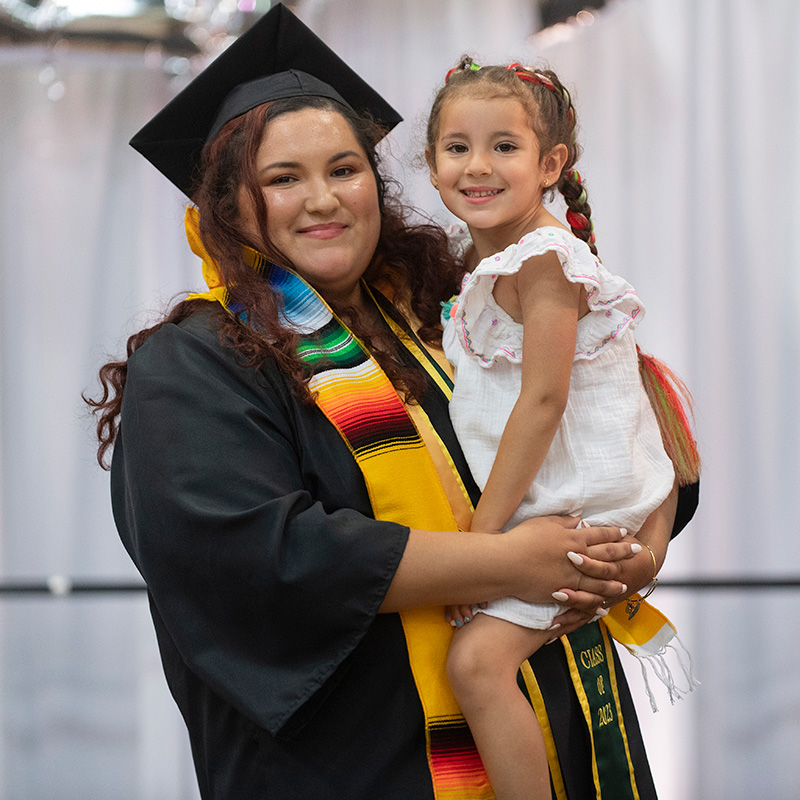 A female graduate holds her daughter during the Raza graduation