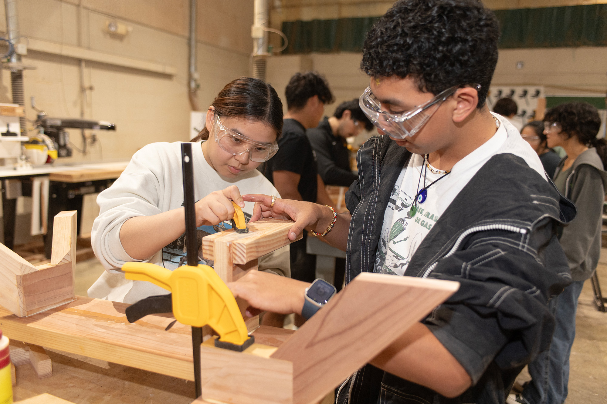 Two carpentry students work on a project with wood.