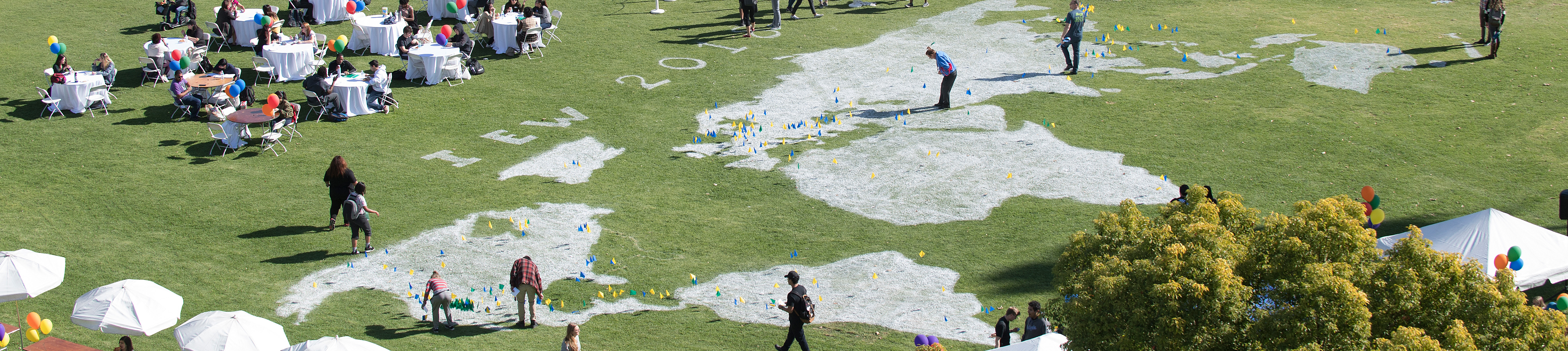 green grass field with an outline of the world map with student walking around