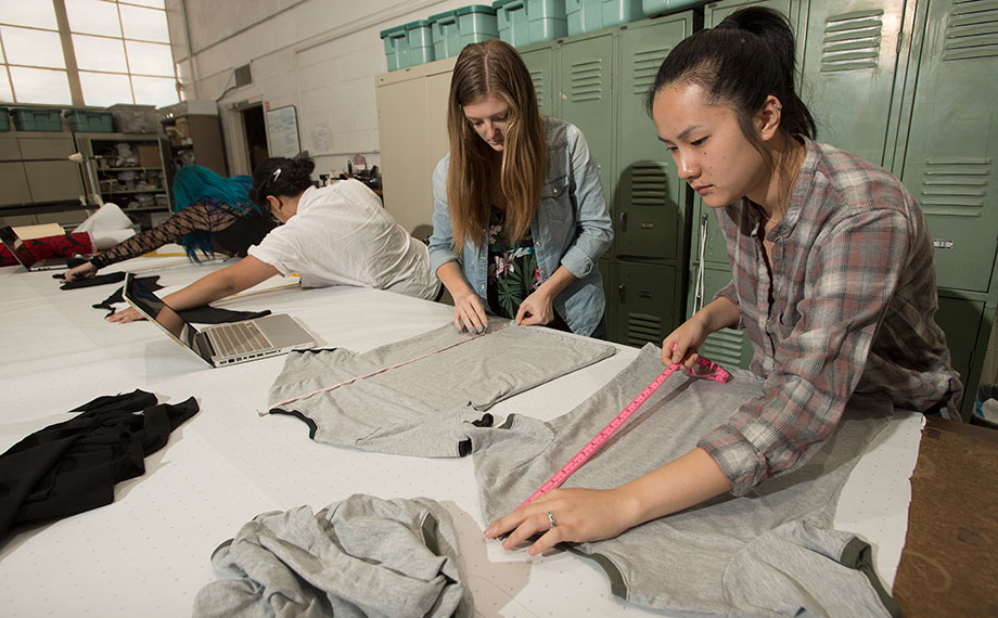 Female students measure garments on a table.