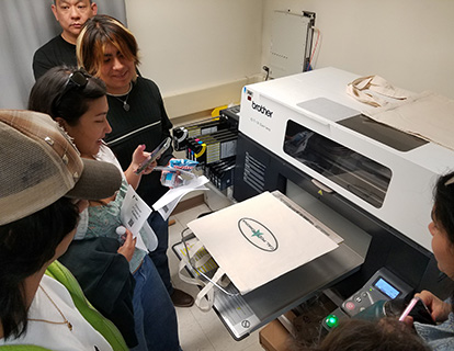 Prospective students watch as a printer prints a design on a garment
