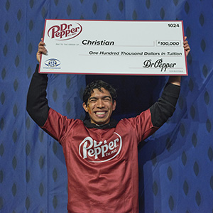 Christian Aguirre holds up a $100,000 check from Dr. Pepper in both hands above his head.