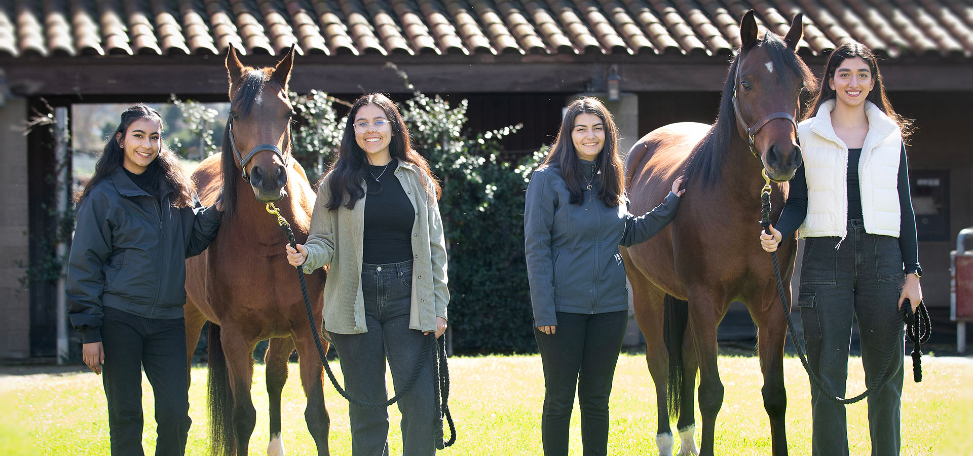 Four students on the team pose with horses