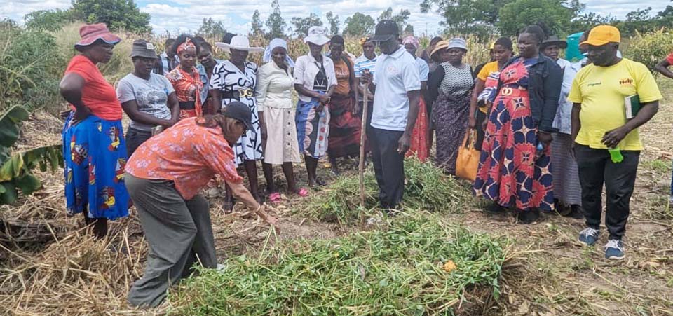 Naveen Hyder kneeling to point something out in a field to a group of students.