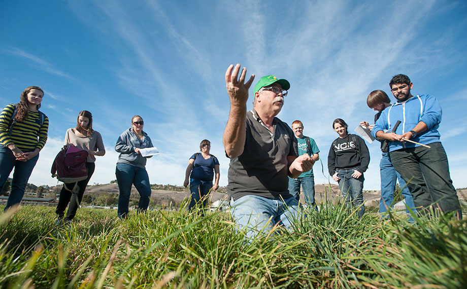Professor Emeritus Dan Hostetler kneels in a pasture as he teaches a group of students.
