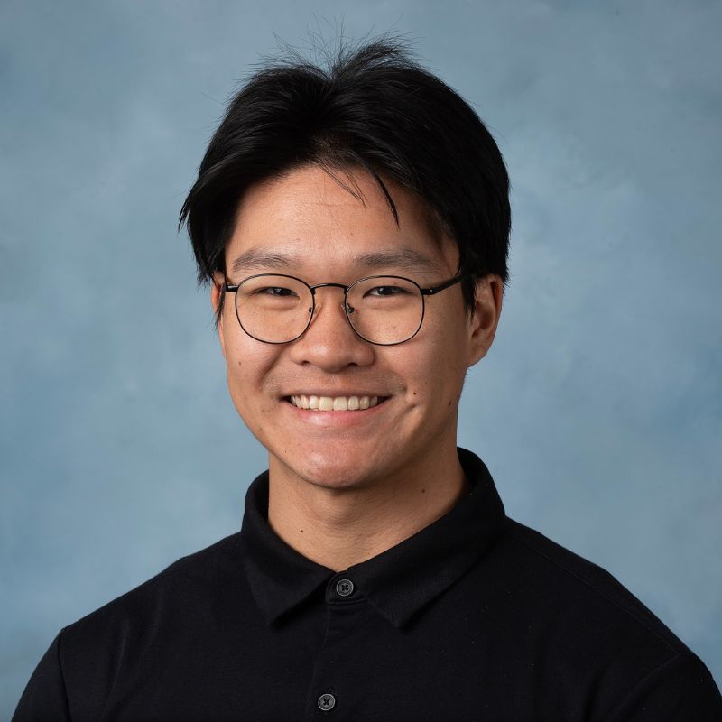 Paulson Cheng wearing glasses and a black polo shirt, smiling against a blue background.