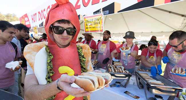 A male student dressed as a hot dog enjoys eating a hot dog during the hot dog caper.