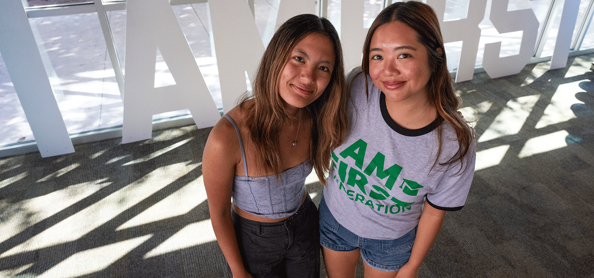 Two female students pose for a photo by the I Am First sign.