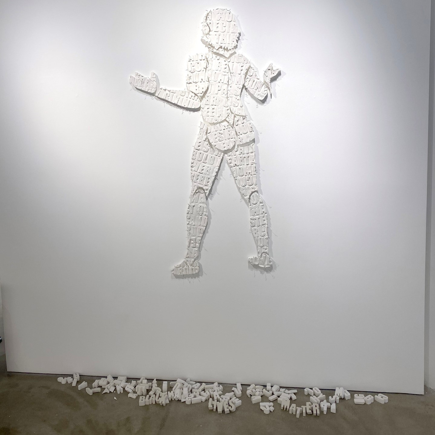 different letters puzzled together to make a human figure in white with their arms out and white letters fallen onto the floor. 