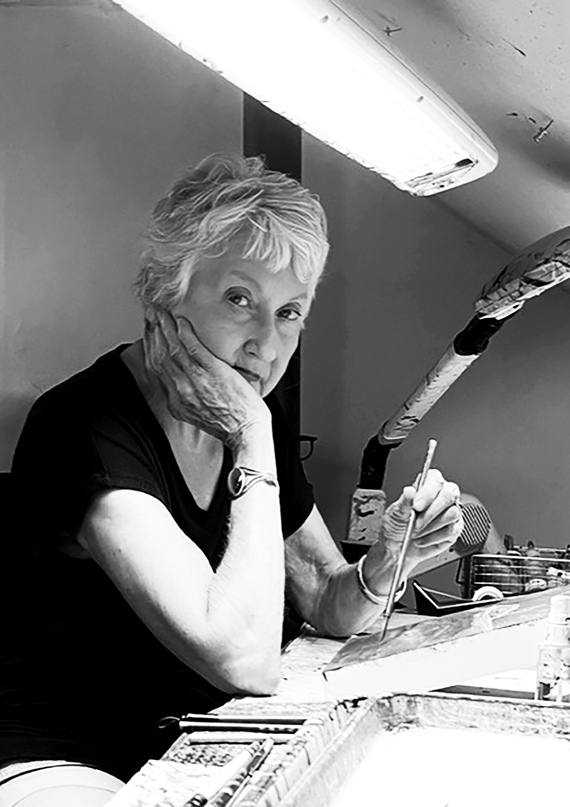 Barbara Thomason, she is wearing a black tee shirt and is sitting at an art workstation with ink and sculpting tools.