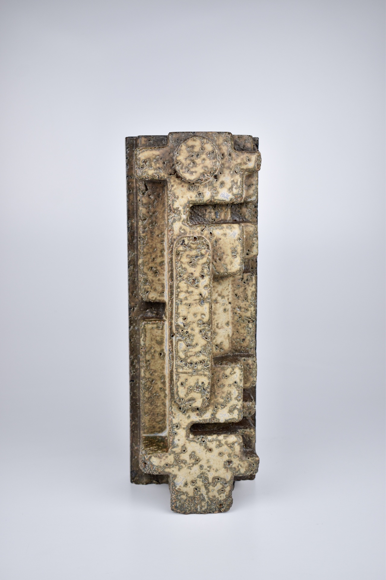  A tall, rectangular ceramic sculpture with textured surfaces and raised geometric patterns, featuring earthy tones and a weathered appearance that evokes a sense of ancient or industrial design.