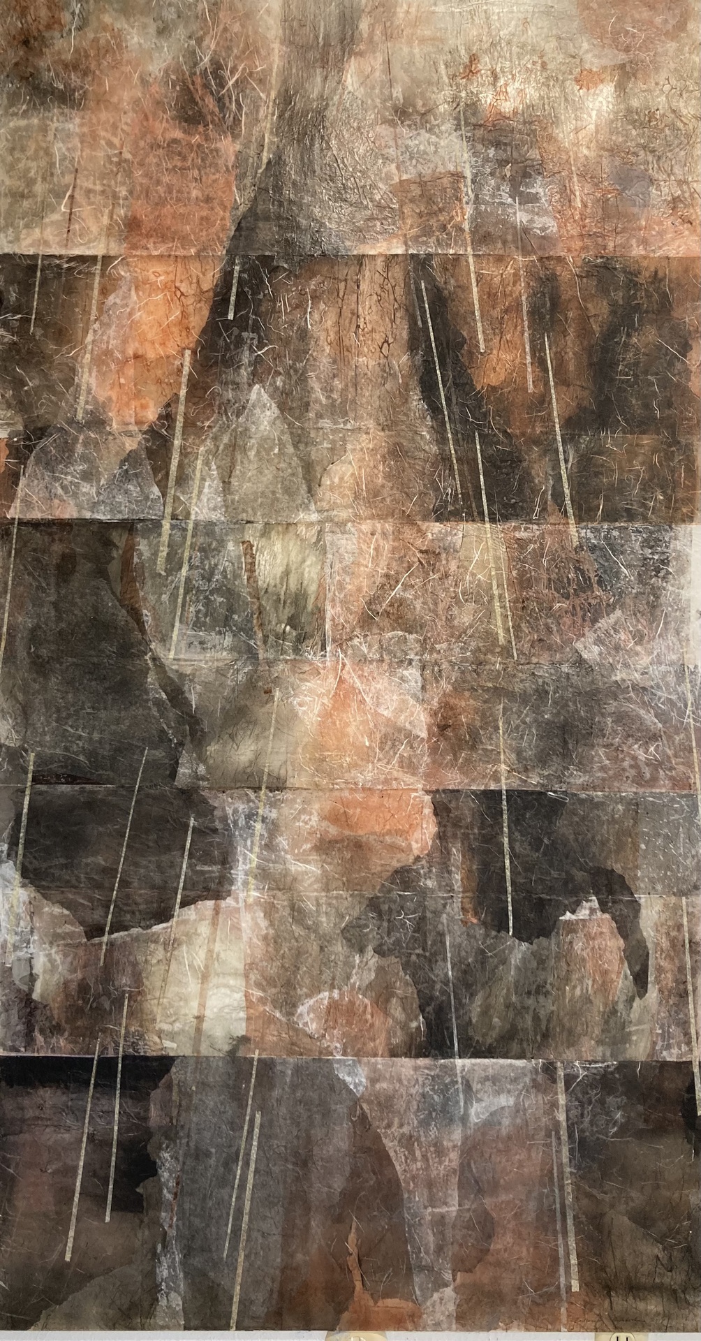 An abstract artwork composed of layered, textured materials in earthy tones of brown, gray, and orange, with streaks of white creating vertical lines that evoke the appearance of rain or light, giving the piece a sense of depth and movement.