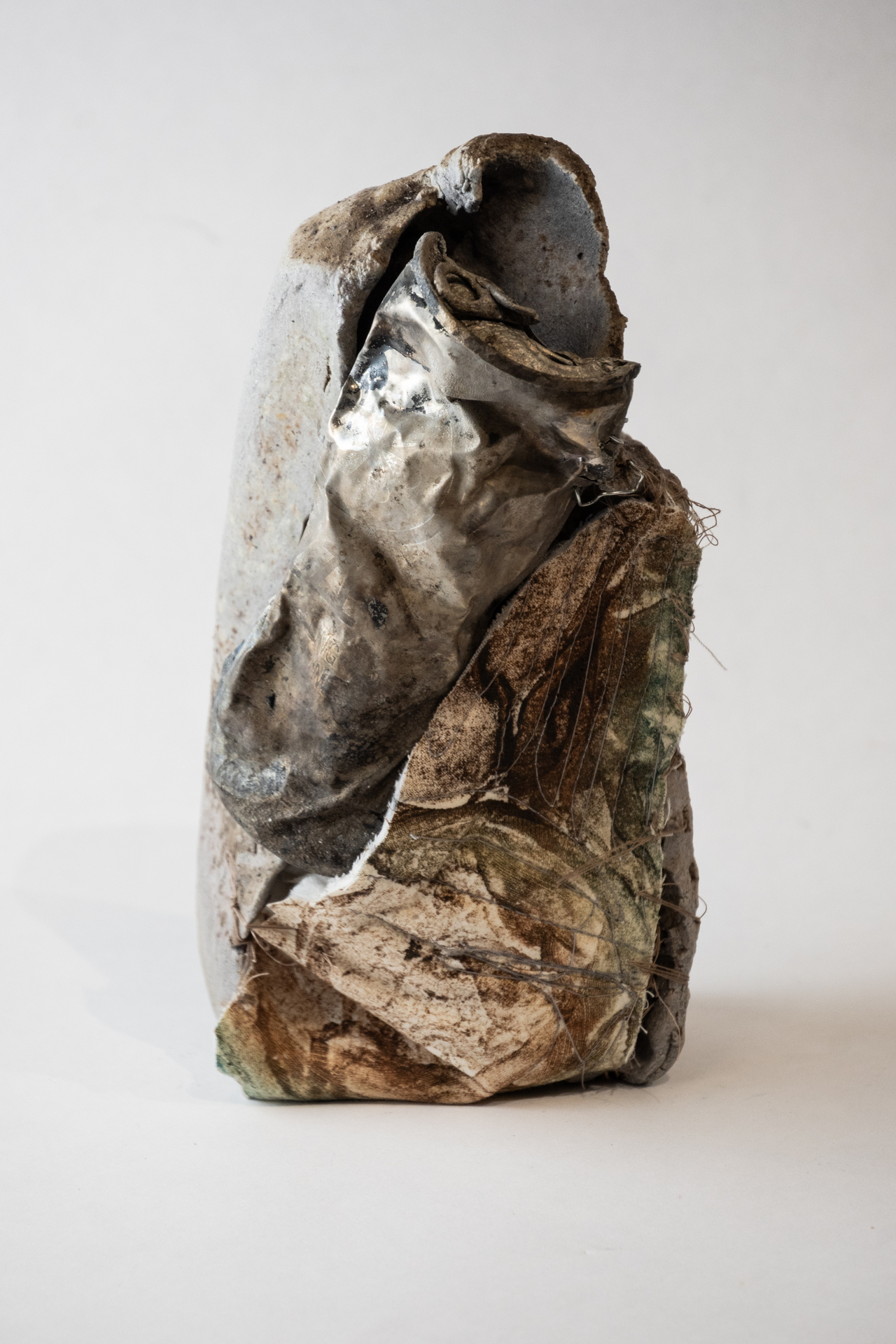 A crumpled, abstract sculpture with layers of textured materials in various shades of brown and silver.