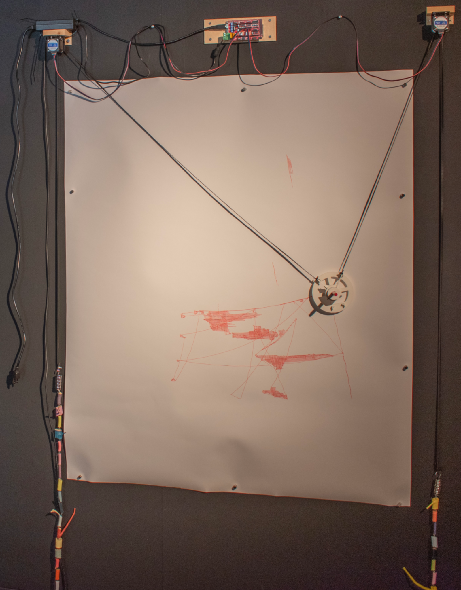 A vertical plotter featuring a robotic mechanism with strings and motors creating red abstract lines on a paper sheet.