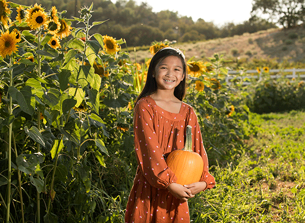 A young girl poses for a photo by the sunflowers