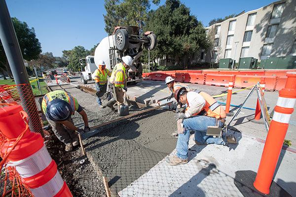 Workers pour a new sidewalk along University Drive