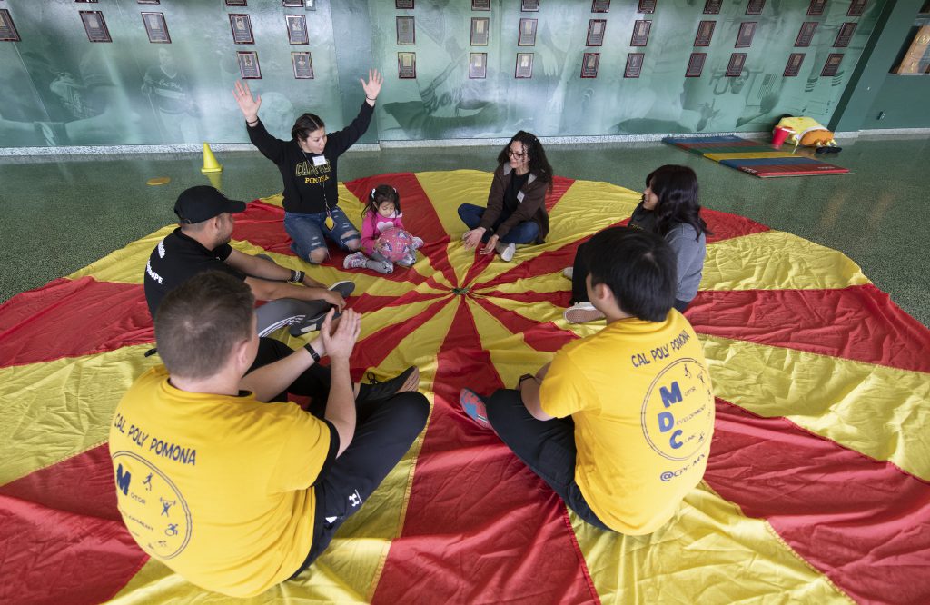 A group of children sit on a parachute with a therapist.