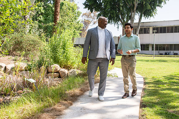 Bryant Fairley walks along campus while speaking with a male student.
