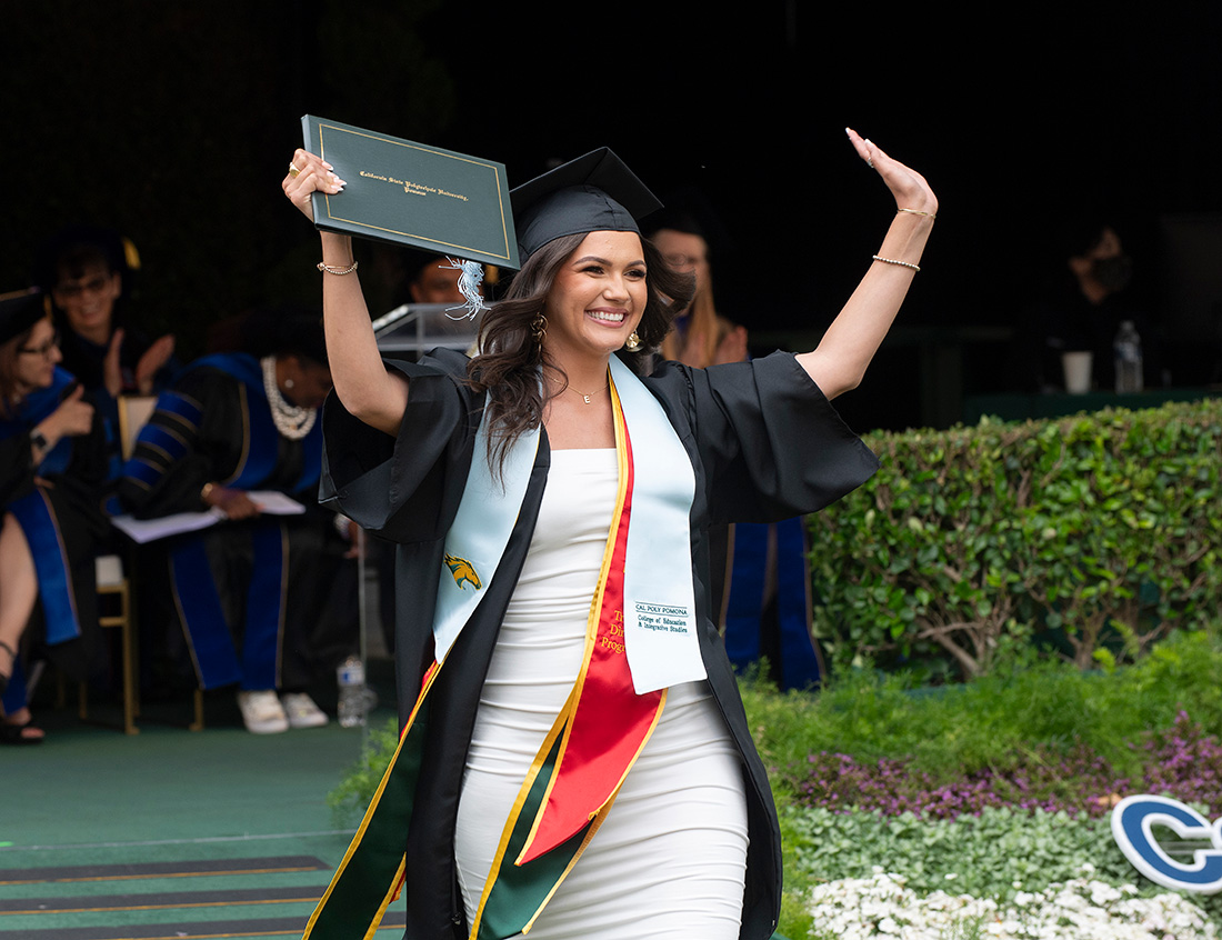 Female graduate holds up her diploma while exiting the commencement stage.