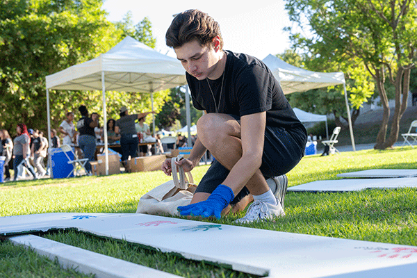 Male student uses paint to leave his handprint on CPP letters.