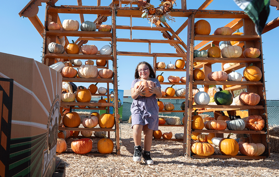 A young gir holds a pumpkin walking through the pumpkin house.