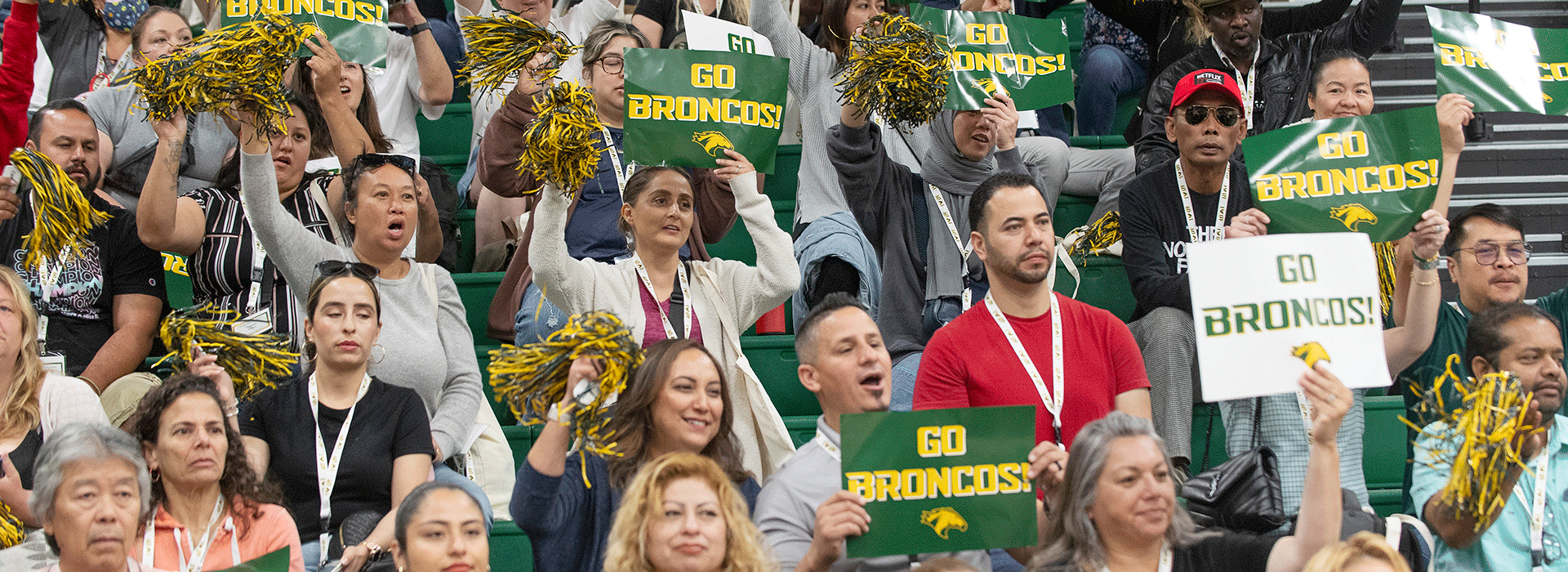 A group of parents cheer in Kellogg Arena holding "Go Broncos!" signage.