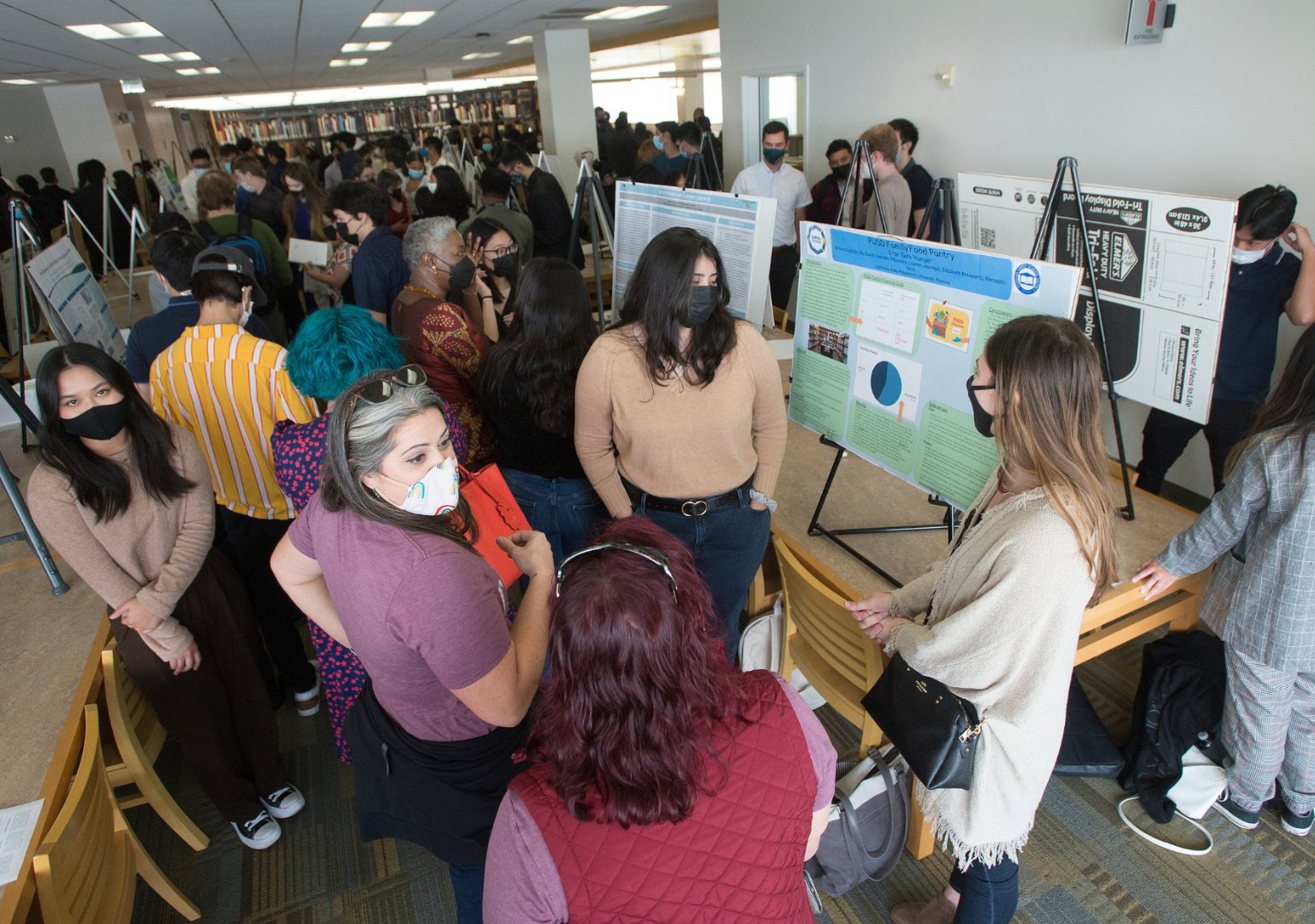 Group of students, presenters and audience members, having a discussion over a project poster at the PolyX showcase event.