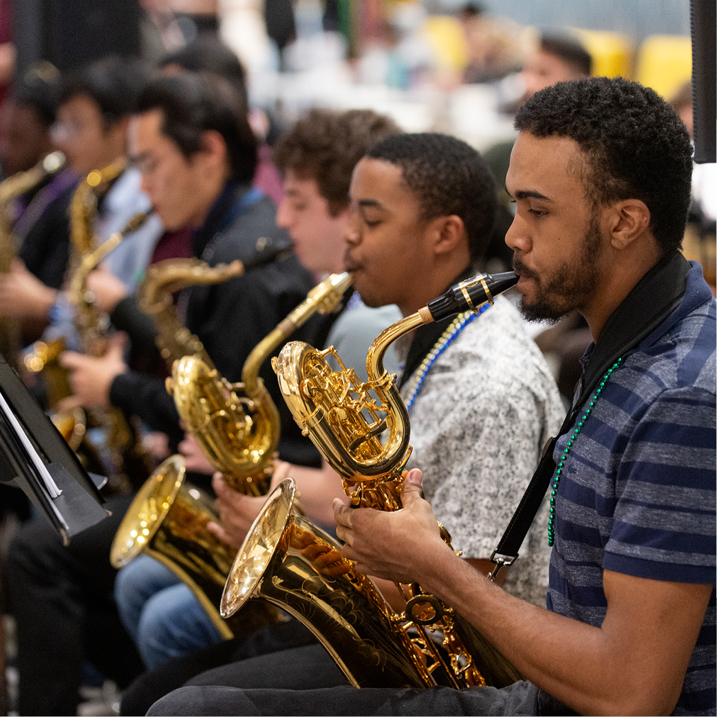 A pair of students, with more students in the background, playing saxophones